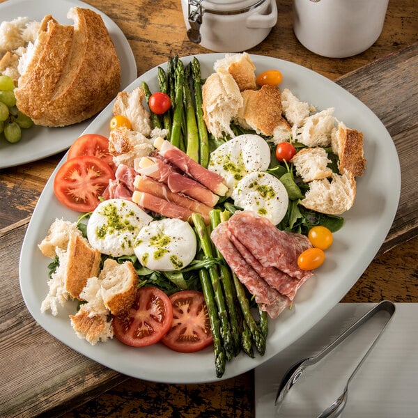 A Carlisle cement melamine oblong platter with asparagus, tomatoes, and bread on a table.