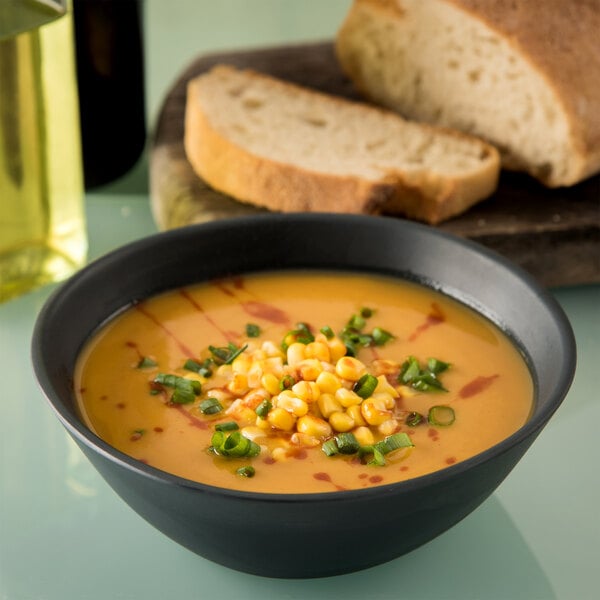 A Carlisle slate melamine bowl filled with soup, corn, and chives on a table.