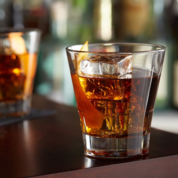 Two Libbey double old fashioned glasses of whiskey with ice on a bar.