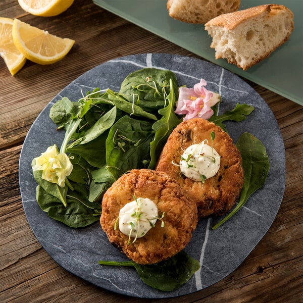 A Carlisle Ridge melamine plate with two fish cakes, salad, and a lemon wedge.