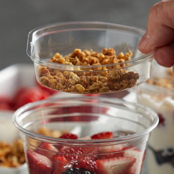 A hand holding a clear plastic cup with granola and yogurt.