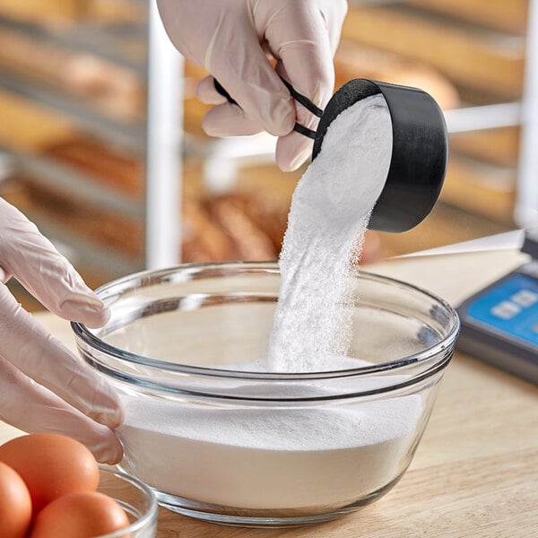 A gloved hand pouring Dextrose Corn Sugar into a bowl.