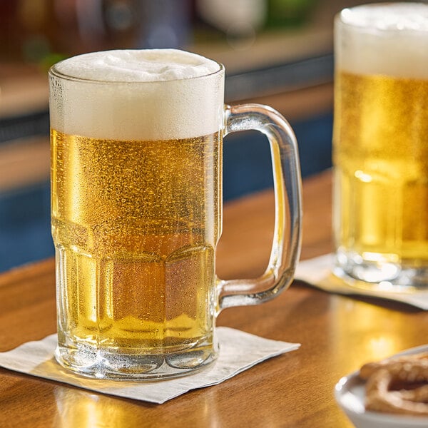 Two Anchor Hocking beer mugs filled with beer on a table with pretzels.