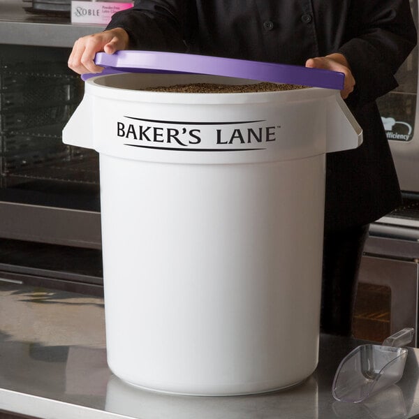 A woman holding a large white Baker's Lane ingredient storage container with a purple lid.