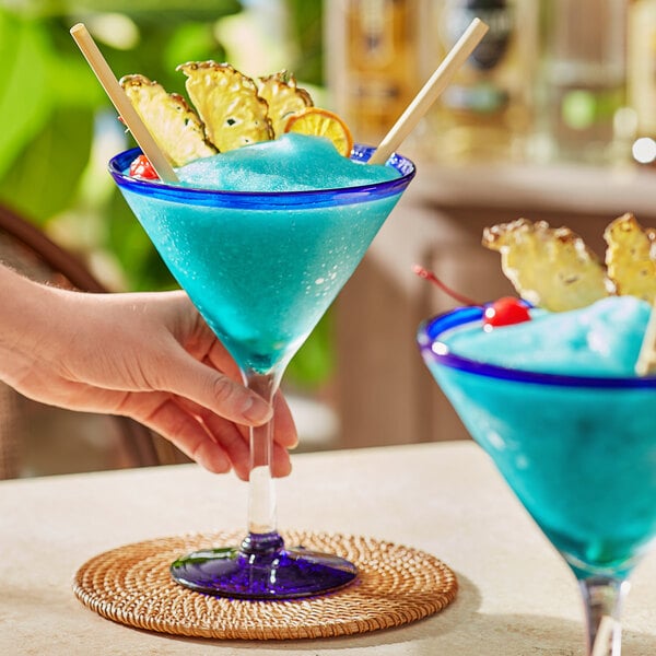 A person holding a blue Acopa Tropic martini with pineapple garnish.