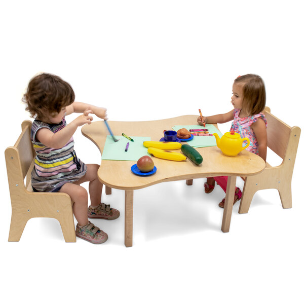 Two children sitting at a flower shaped wooden table drawing with crayons.