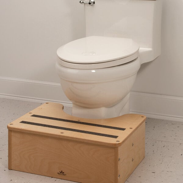 A white toilet with a Whitney Brothers wooden step stool next to it.