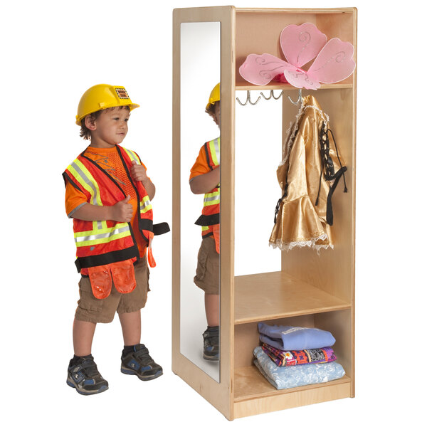 A boy wearing a hard hat and safety vest standing next to a Whitney Brothers dress up wardrobe with a mirror.
