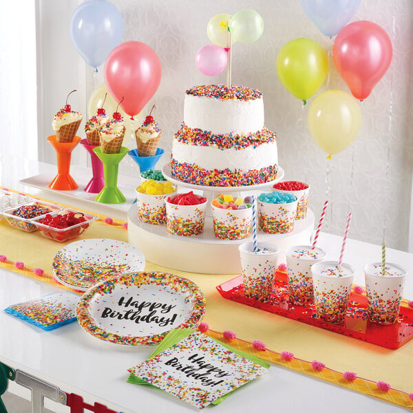 A Creative Converting paper hot cup with sprinkles on it next to a cake on a table.