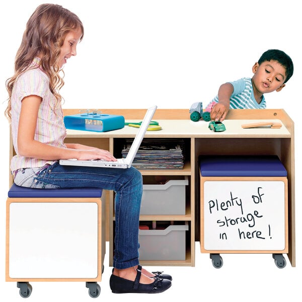 A girl sitting at a Whitney Brothers STEM activity desk using a laptop.