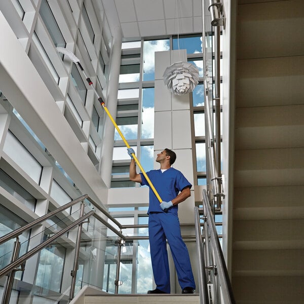 A man in blue scrubs using a Rubbermaid yellow telescoping handle on a mop.