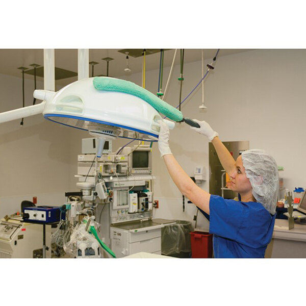 A person using a Rubbermaid HYGEN Quick-Connect Flexi-Wand with a green microfiber dusting sleeve to clean medical equipment in a hospital setting.