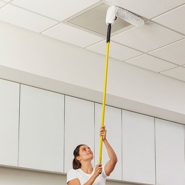 A person using a long-handled duster with a white microfiber dusting sleeve to clean a ceiling vent.