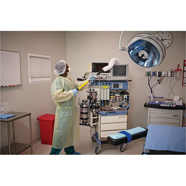 A person using a Rubbermaid HYGEN Executive Series Quick-Connect Flexi-Wand with a white microfiber dusting sleeve to clean medical equipment in a hospital room.