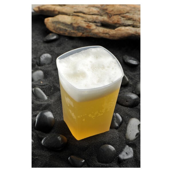 A Fineline clear plastic tumbler filled with beer and foam on black rocks.