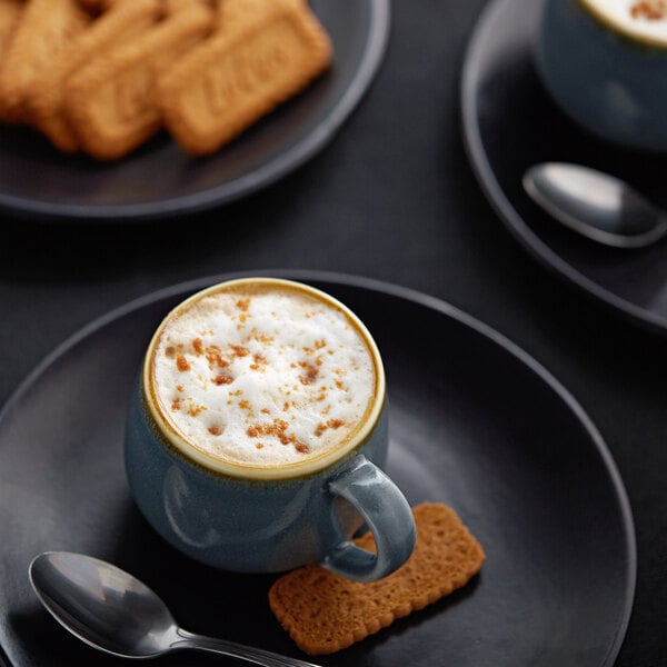 A cup of coffee with foam and Torani Sugar-Free Belgian Cookie flavoring syrup on a spoon.