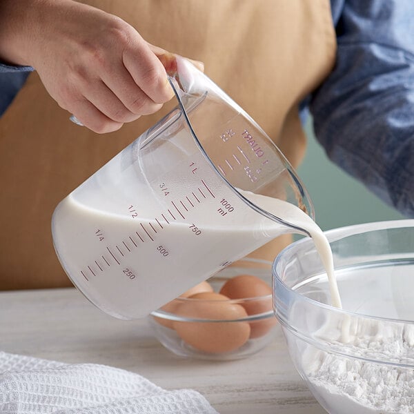 A person pouring flour into a bowl using a purple measuring cup.