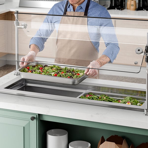 A man in an apron preparing food at a Delfield narrow drop-in cold food well.