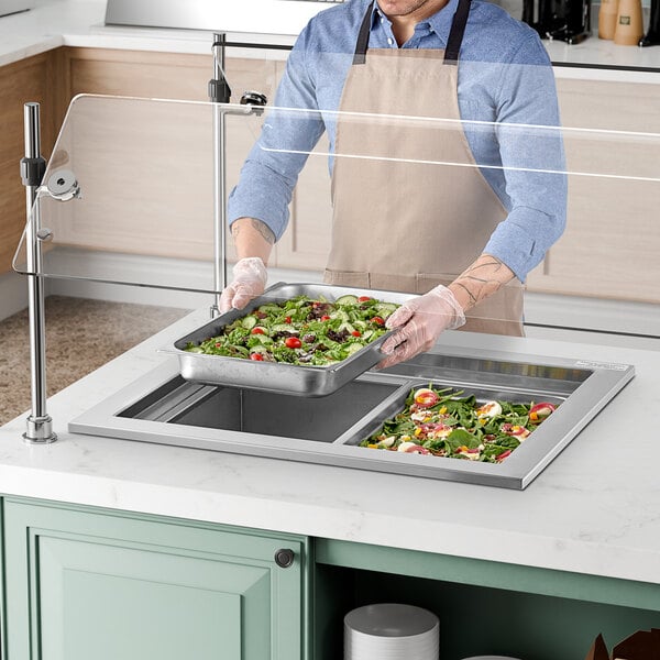A man in an apron using a Delfield drop-in cold food well to prepare a salad on a counter.