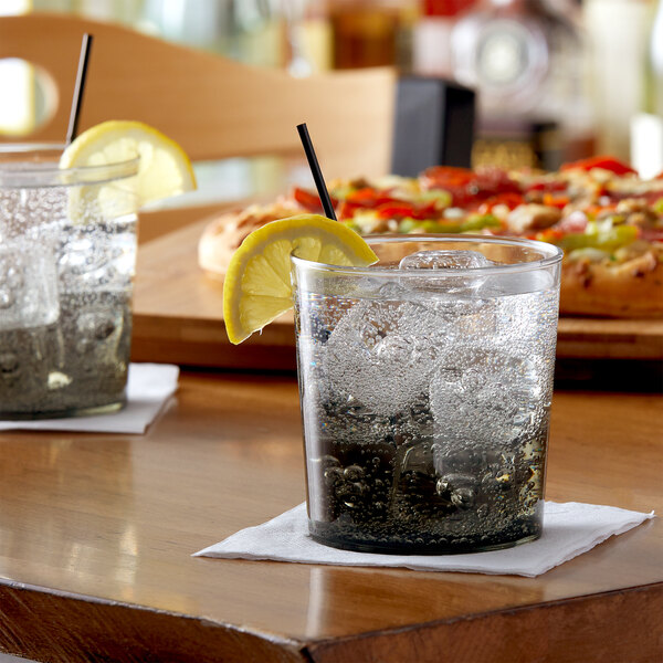 A glass with ice and a slice of lemon on a table with other glasses.