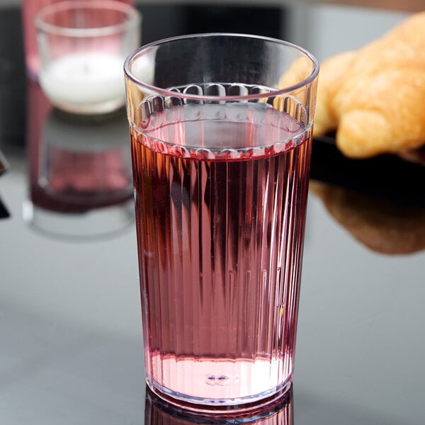 A Carlisle clear plastic tumbler filled with pink liquid on a table.