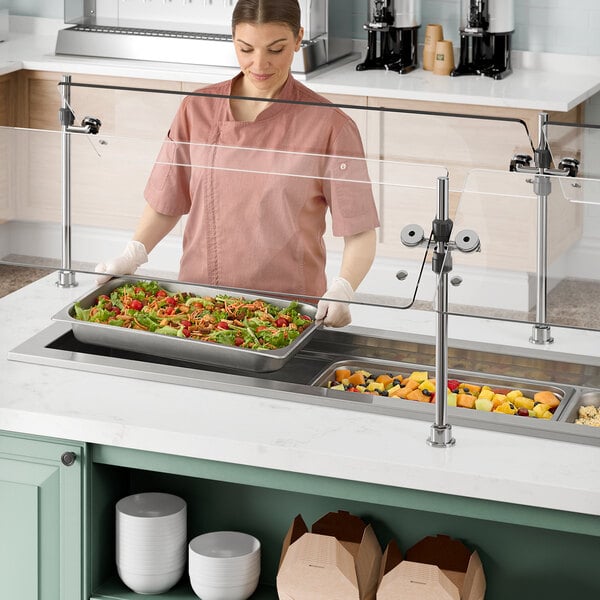 A woman in pink scrubs using a Delfield narrow drop in cold food well to serve food.