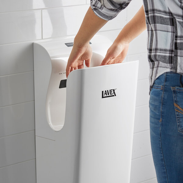 A woman using a Lavex high speed vertical hand dryer with a white surface.