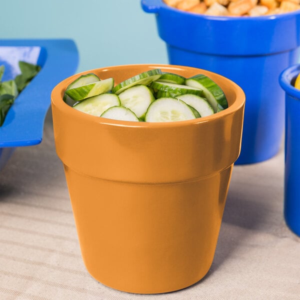 An orange Tablecraft round condiment bowl filled with cucumbers on a table.