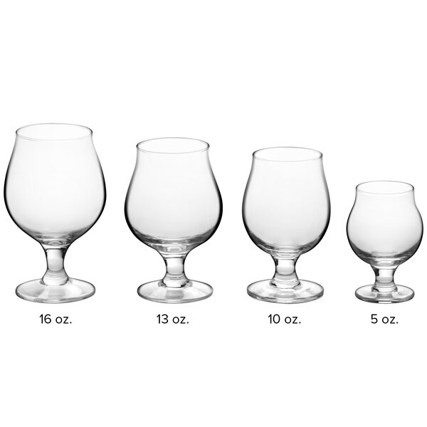 A row of clear Acopa Select tulip glasses with a white liquid in one.