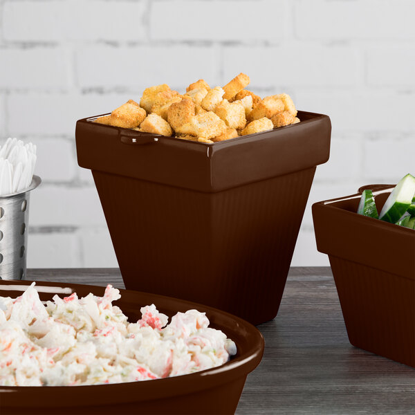 A table with three brown Tablecraft cast aluminum square condiment bowls filled with food.