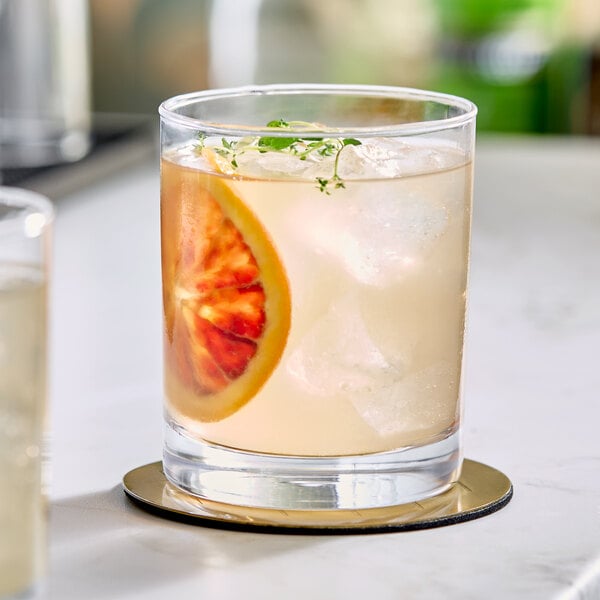 A clear 12 oz. rocks glass filled with a light-colored beverage, ice, a slice of citrus, and a garnish, sitting on a coaster.