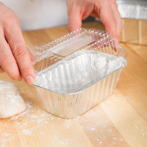 A person's hand placing dough into a clear plastic dome lid.
