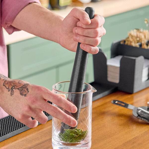 A person using a Barfly black composite muddler in a beaker.