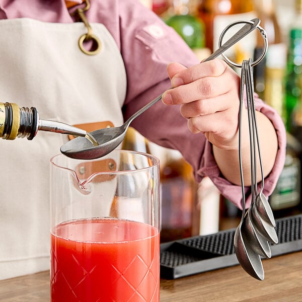 A person using a Barfly stainless steel bar spoon to pour liquid into a glass.