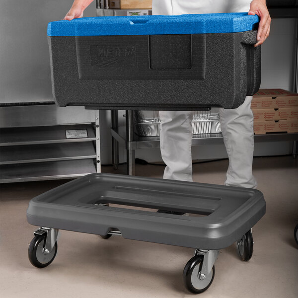 A man using a black and blue Metro Mightylite food pan carrier on a cart.