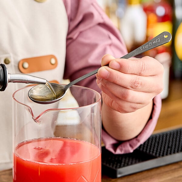 A person using a Barfly stainless steel measuring spoon to pour liquid into a glass.