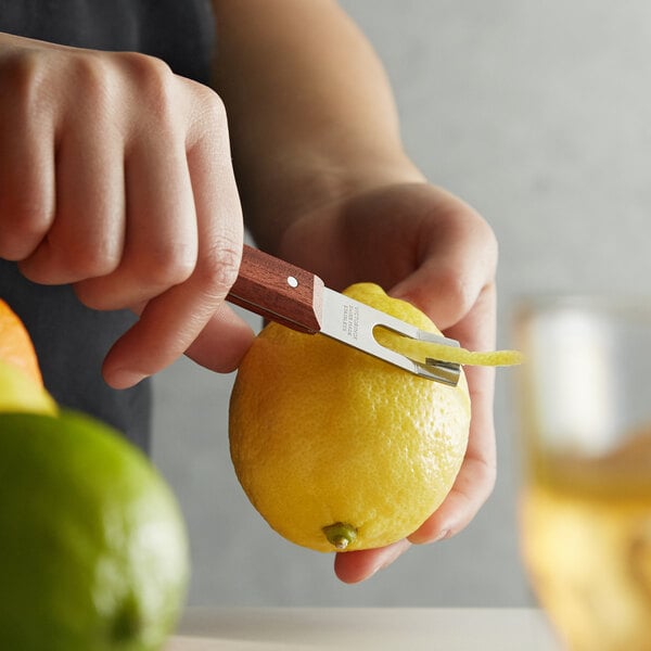 A person using a Victorinox channel knife with a rosewood handle to peel a lemon over a counter.