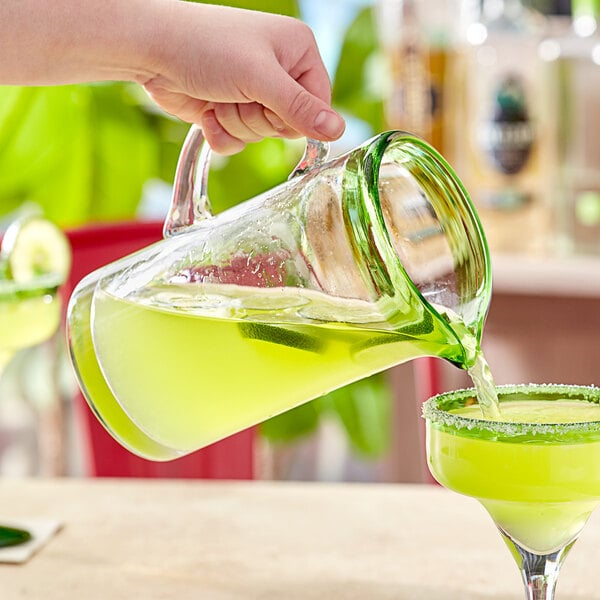 A hand pouring green liquid from an Acopa Tropic glass pitcher into a glass.