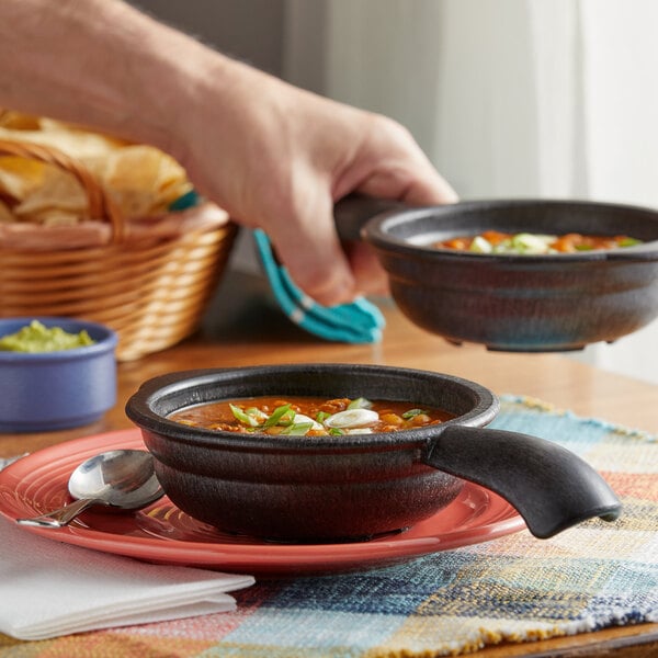 A person holding a pair of HS Inc. charcoal polypropylene serving bowls filled with soup.