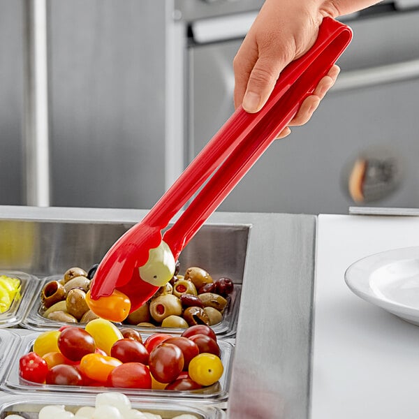 A person holding a Carlisle red plastic utility tong to a bowl of olives.