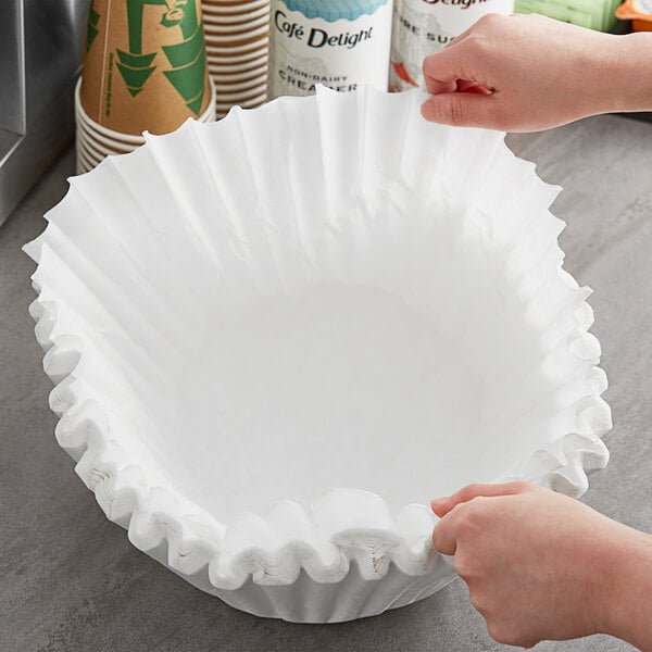 A hand holding a white paper coffee filter.