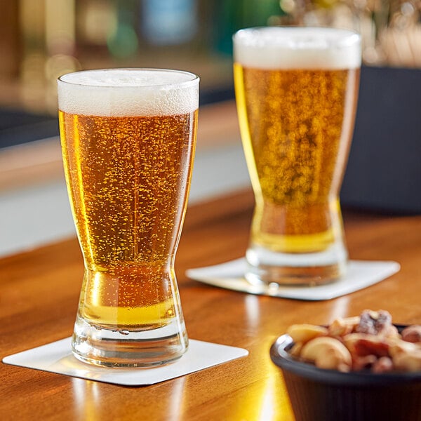 Two Libbey pilsner glasses of beer on a table.