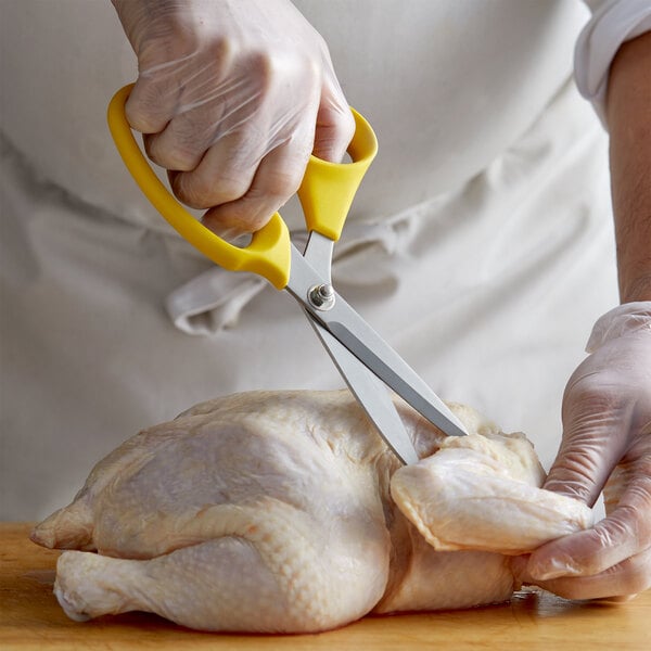 A person in gloves using ARY VacMaster yellow poultry shears to cut a chicken.