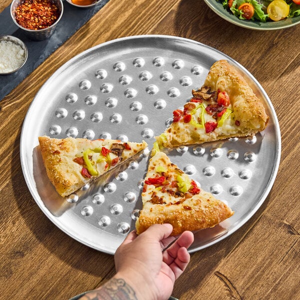 A round, heavy weight aluminum pizza pan with raised nibs, holding three slices of pizza.