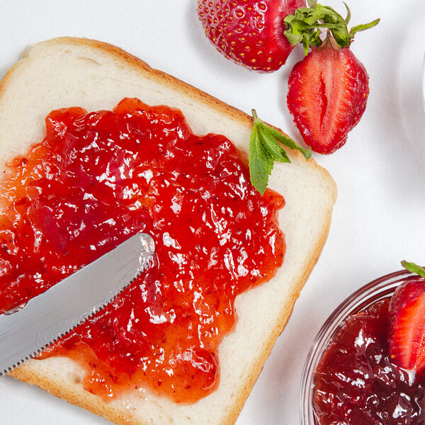 A piece of bread with a knife and Strawberry Jam.