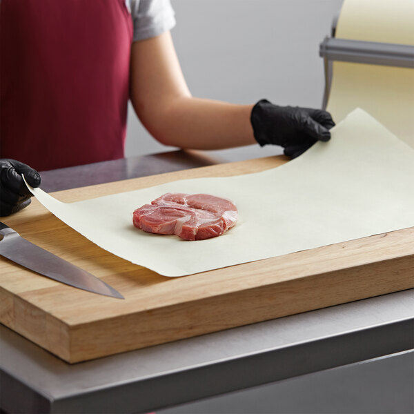 A person in gloves using a knife to cut meat on a Gardenia Premium Paper roll on a cutting board.