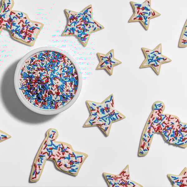 A bowl of red, white, and blue sprinkles surrounded by star and flag-shaped cookies decorated with the same sprinkles.