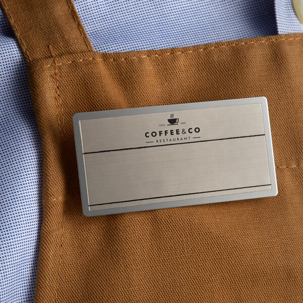 A brown apron with a Cawley silver metal rectangle name tag on it.