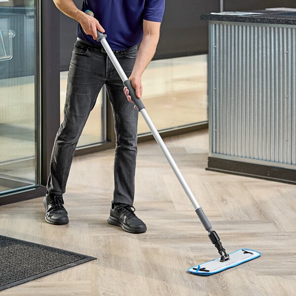 A person using a Lavex Blue Microfiber Spray Mop to clean a floor.