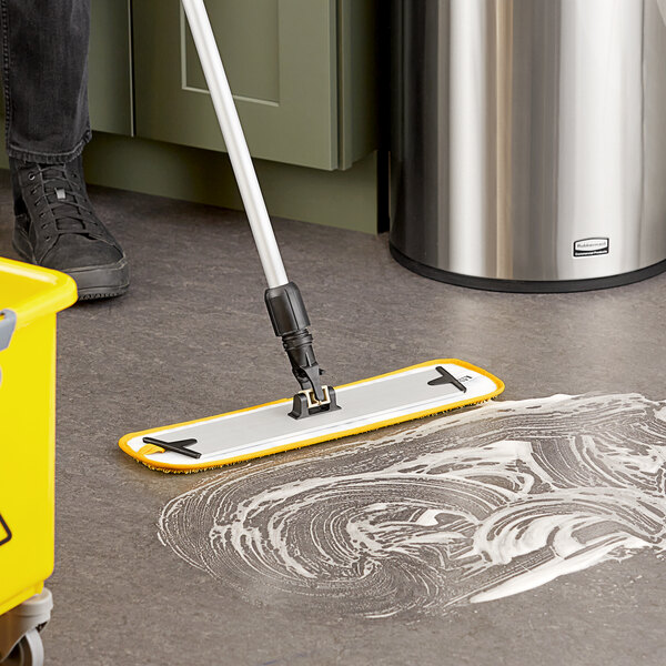 A person using a yellow Lavex microfiber spray mop to clean a floor.